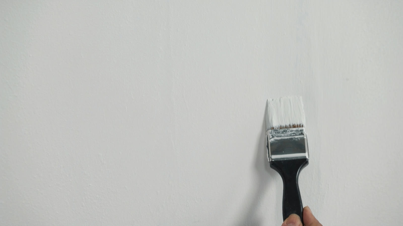 A painter's brush laying a clean, even coat of fresh paint on a smooth white interior wall