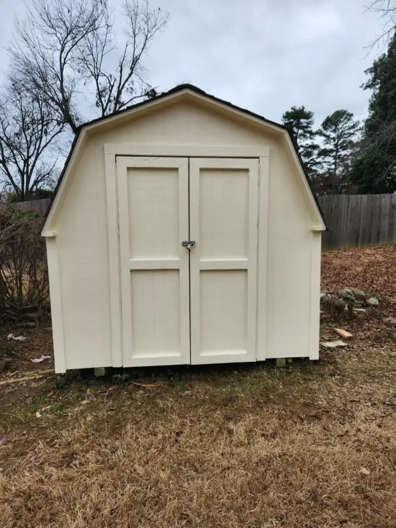 A backyard shed painted cream with white trim and double doors